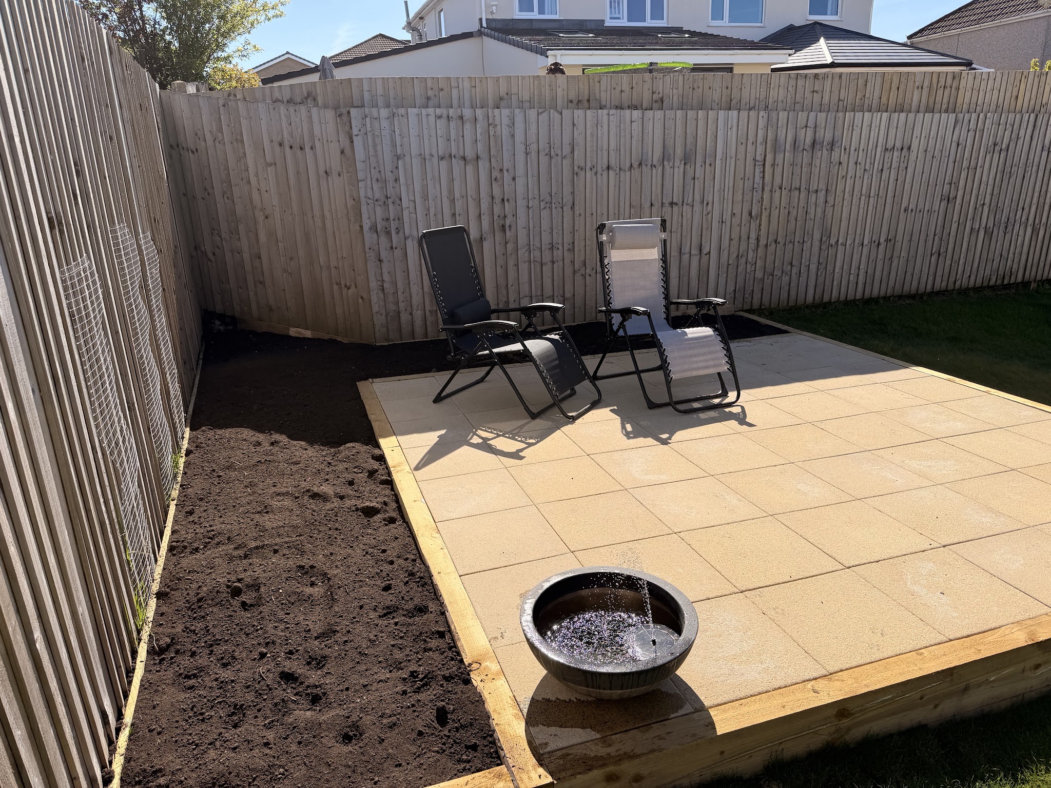 New patio slabs with a timber edge, a fence and two loungers